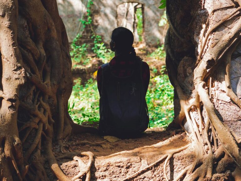 7 Benefits Of A Life Rooted in God Woman sitting inside of opening in tree roots.