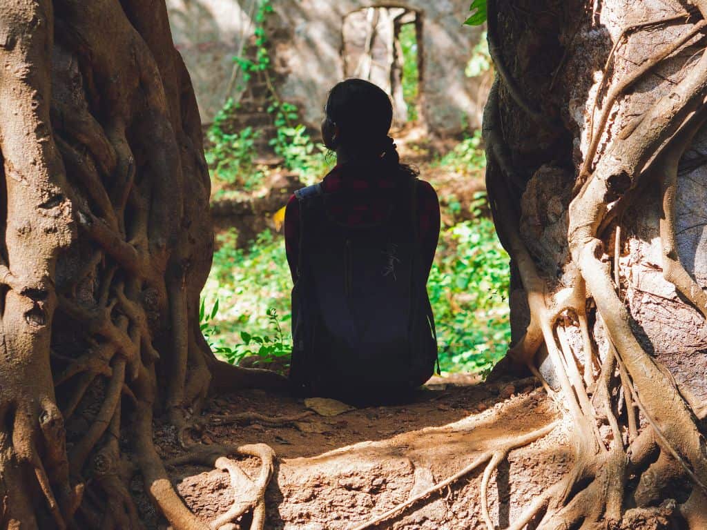 Woman sitting inside of opening in tree roots.