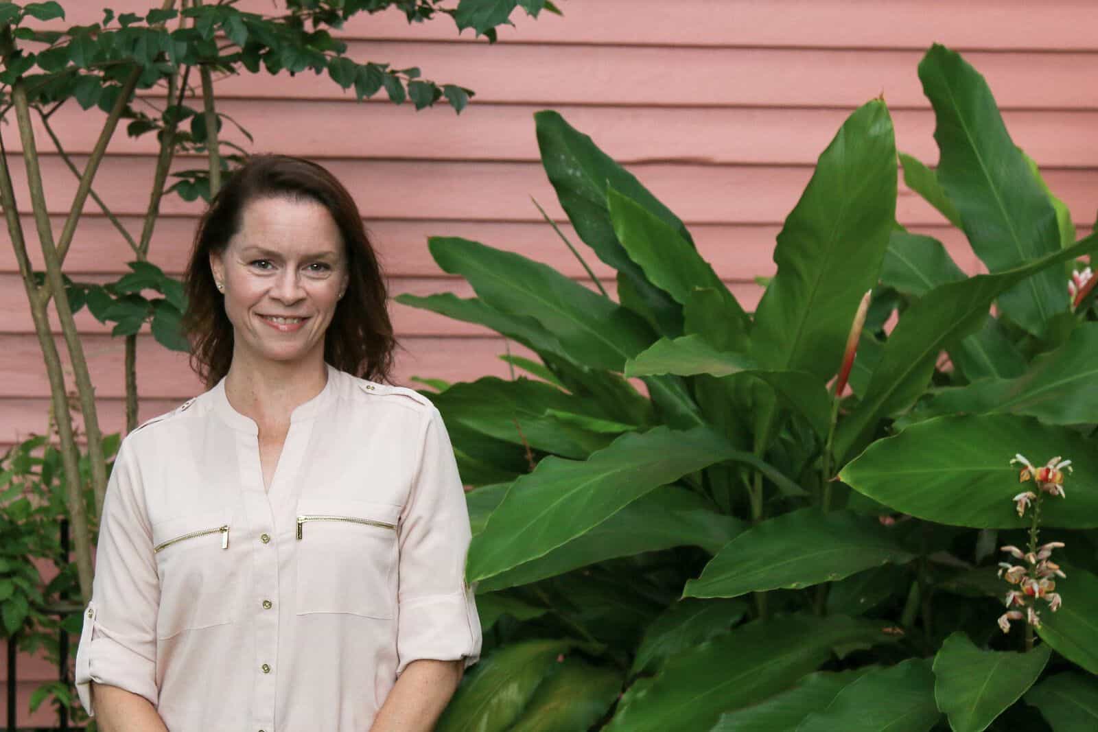 Laurie Darling standing next to a large green plant with a pink building behind.