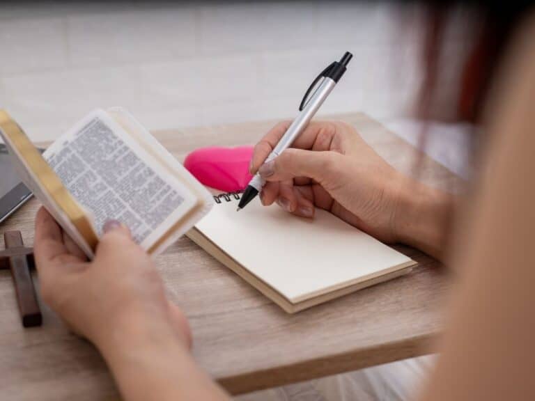 Which Method is Right for You? Understanding Bible Studies, Plans, and Devotionals Person holding small open Bible while writing on a pad of paper.